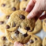 Close view of a hand breaking a chocolate chip cookie in half.