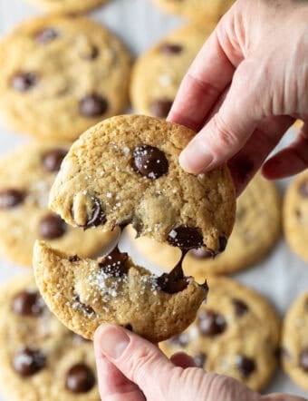 Close view of a hand breaking a chocolate chip cookie in half.