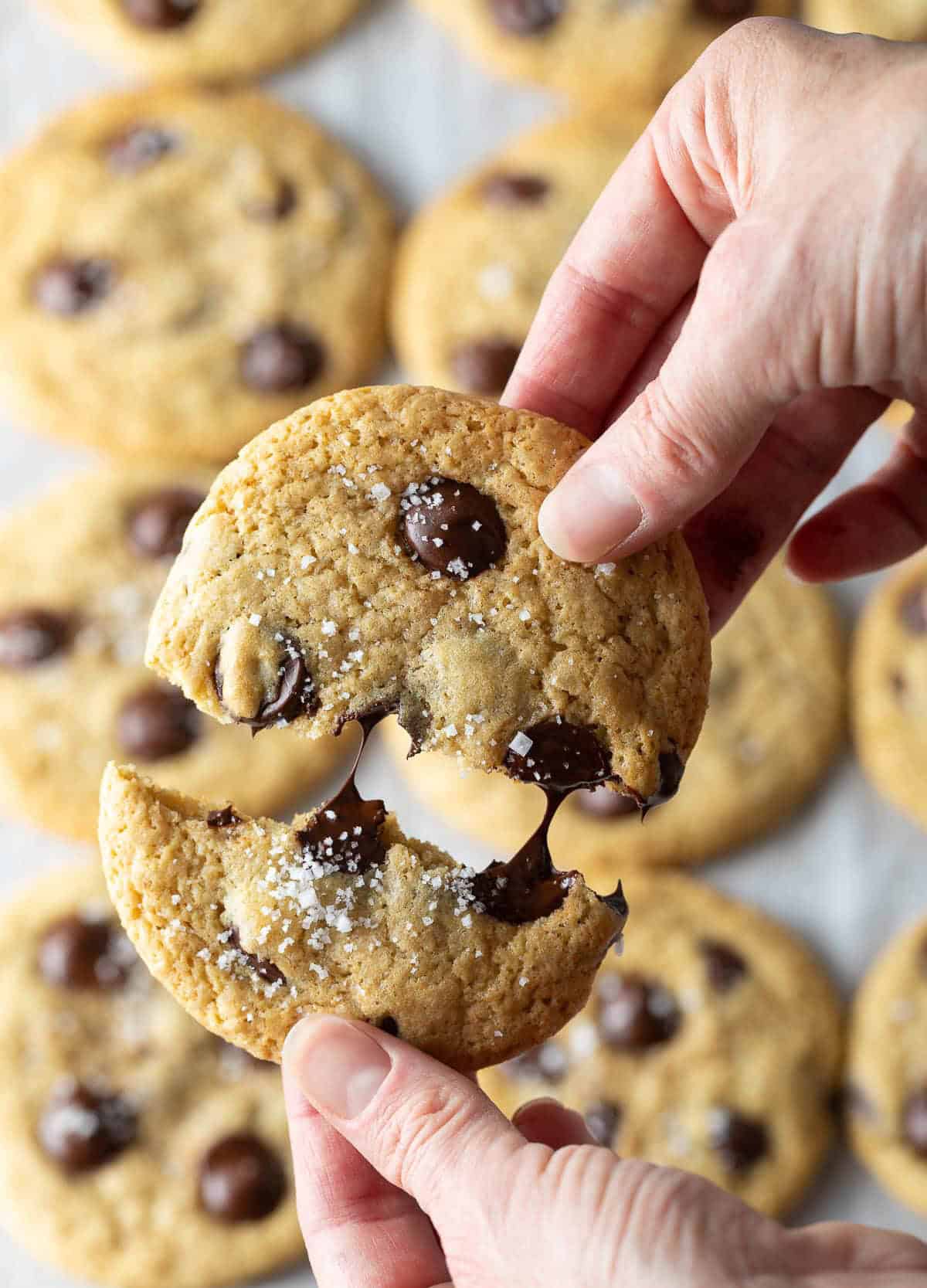 Close view of a hand breaking a chocolate chip cookie in half.