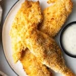 A plate of crispy air fried chicken tenders next to a ramekin of white sauce.