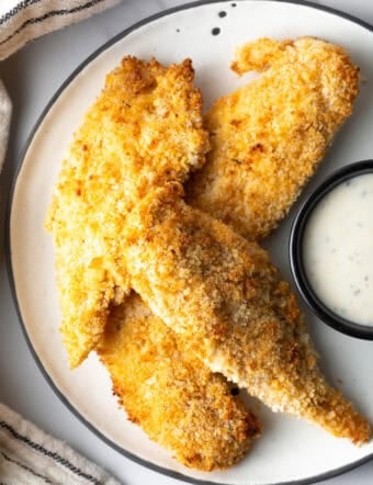 A plate of crispy air fried chicken tenders next to a ramekin of white sauce.