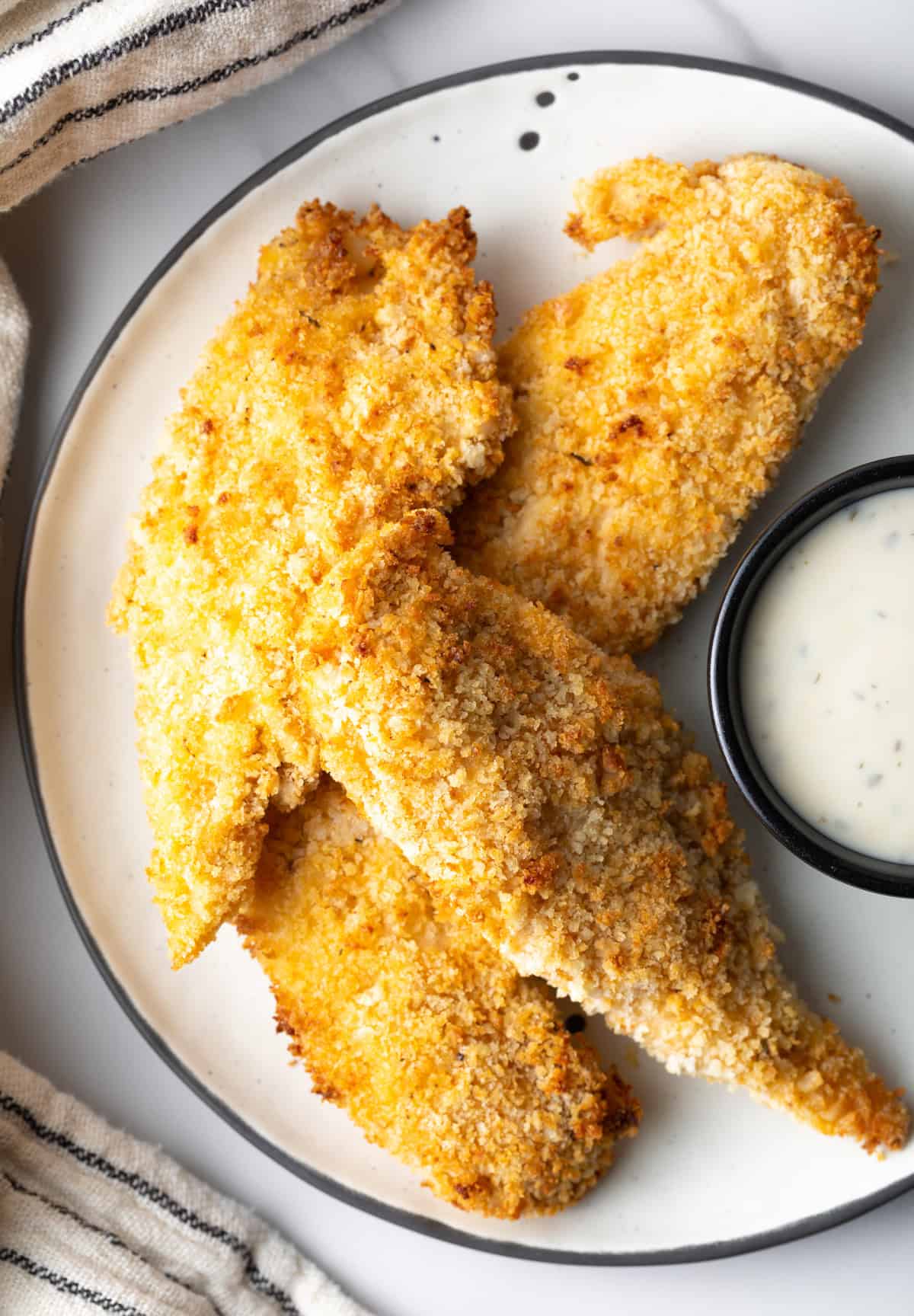 A plate of crispy air fried chicken tenders next to a ramekin of white sauce.