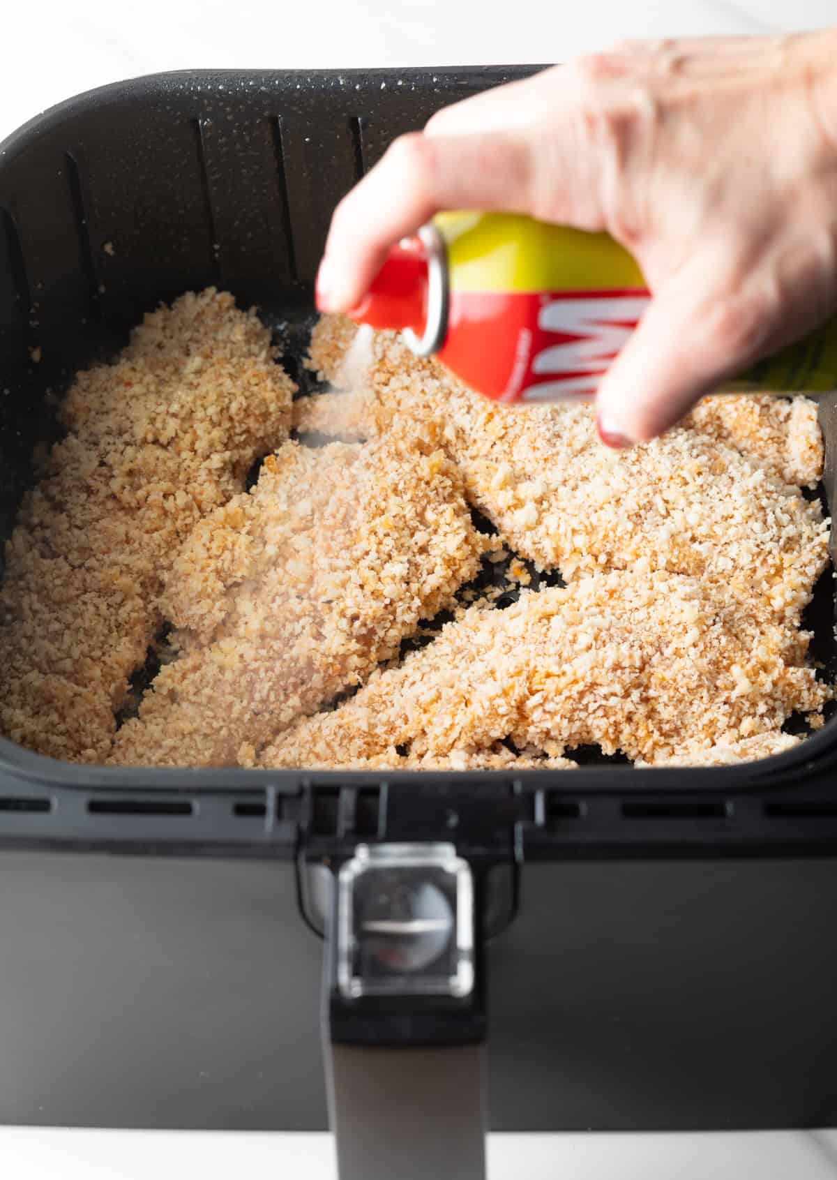 Chicken tenders in the air fryer that are being sprayed with cooking oil.
