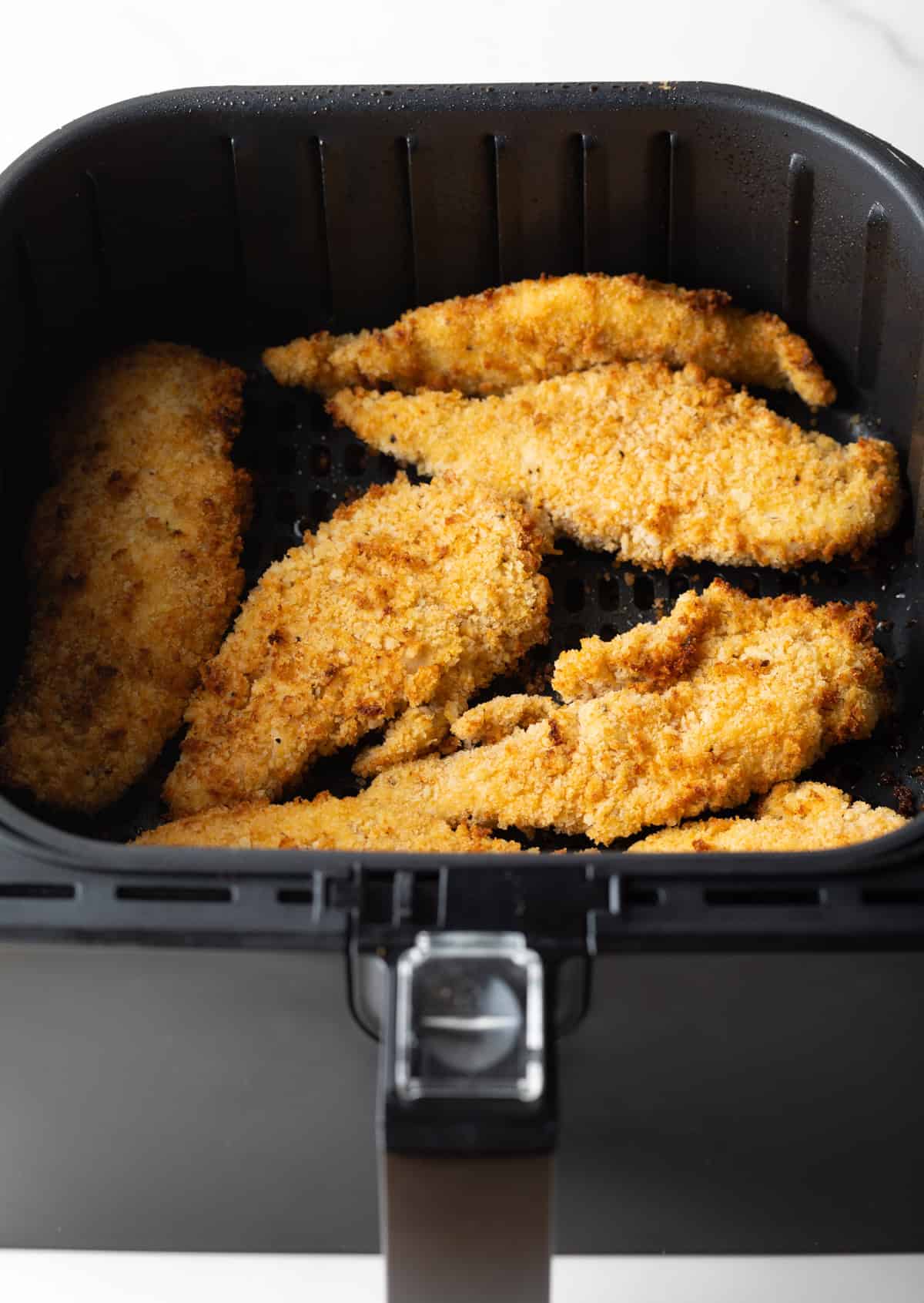 Crispy and golden air fried chicken tenders sitting in an air fryer basket.
