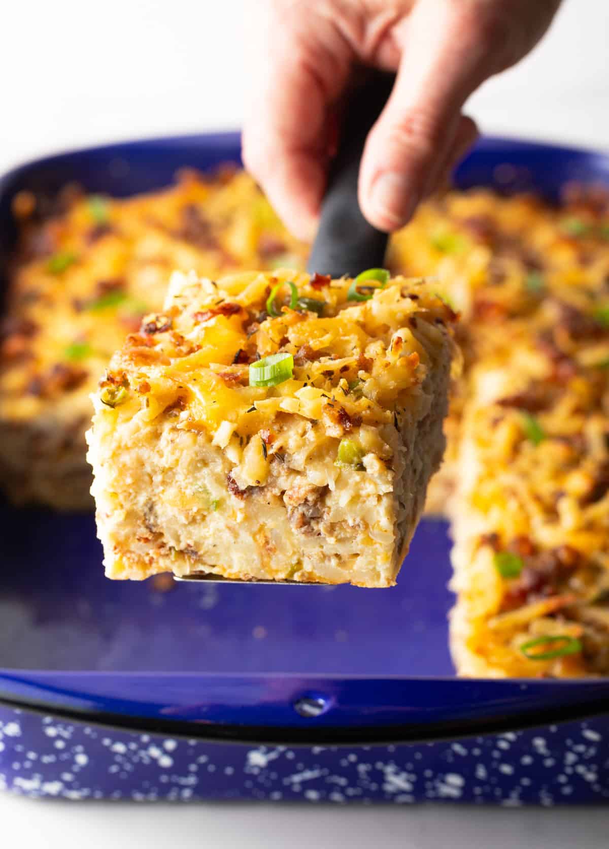 Hand with a square of casserole held towards camera.