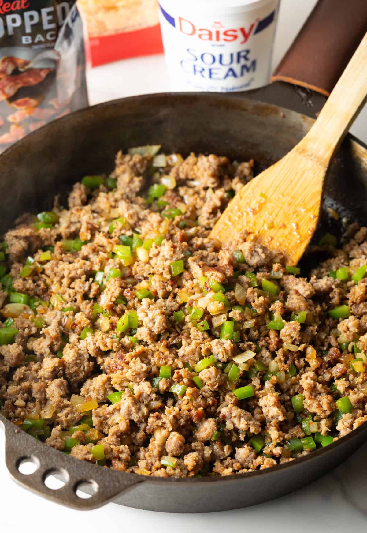 Sausage and vegetables are being cooked in a black pan for a breakfast casserole with hash browns.