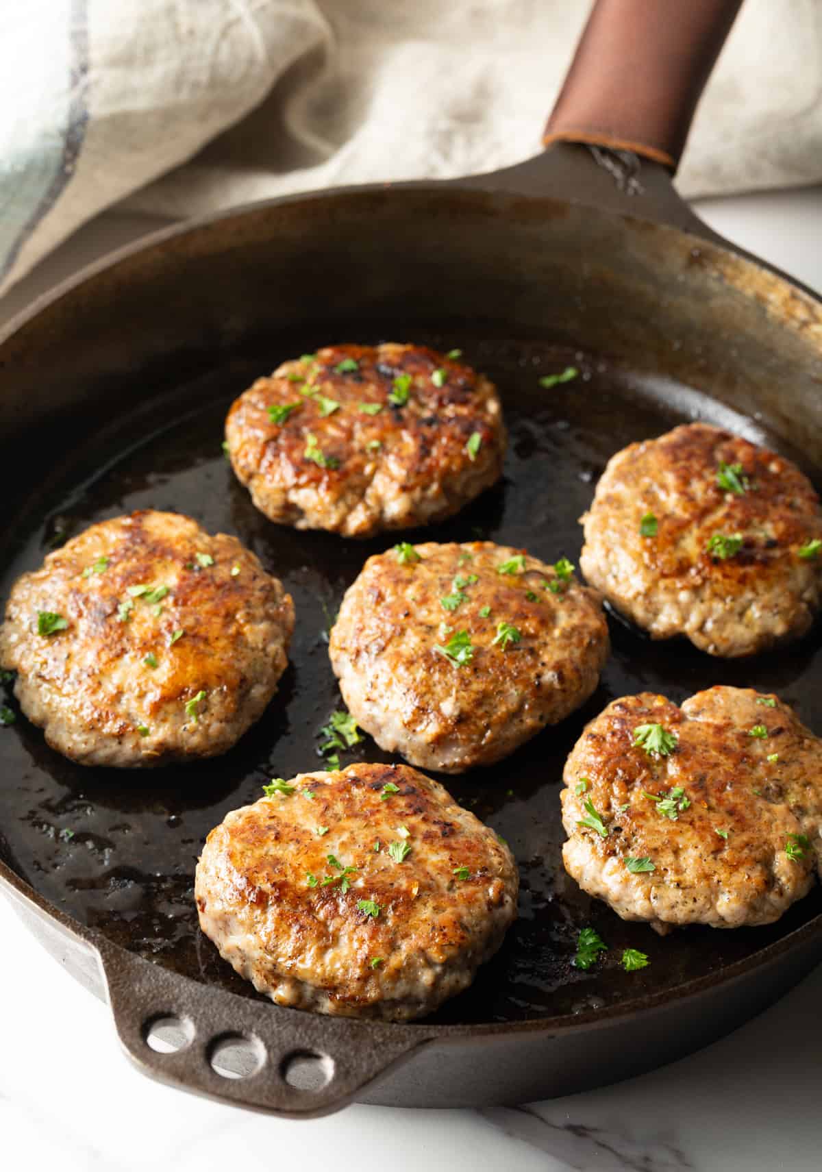 A homemade breakfast sausage recipe is being cooked and browned in a black skillet.
