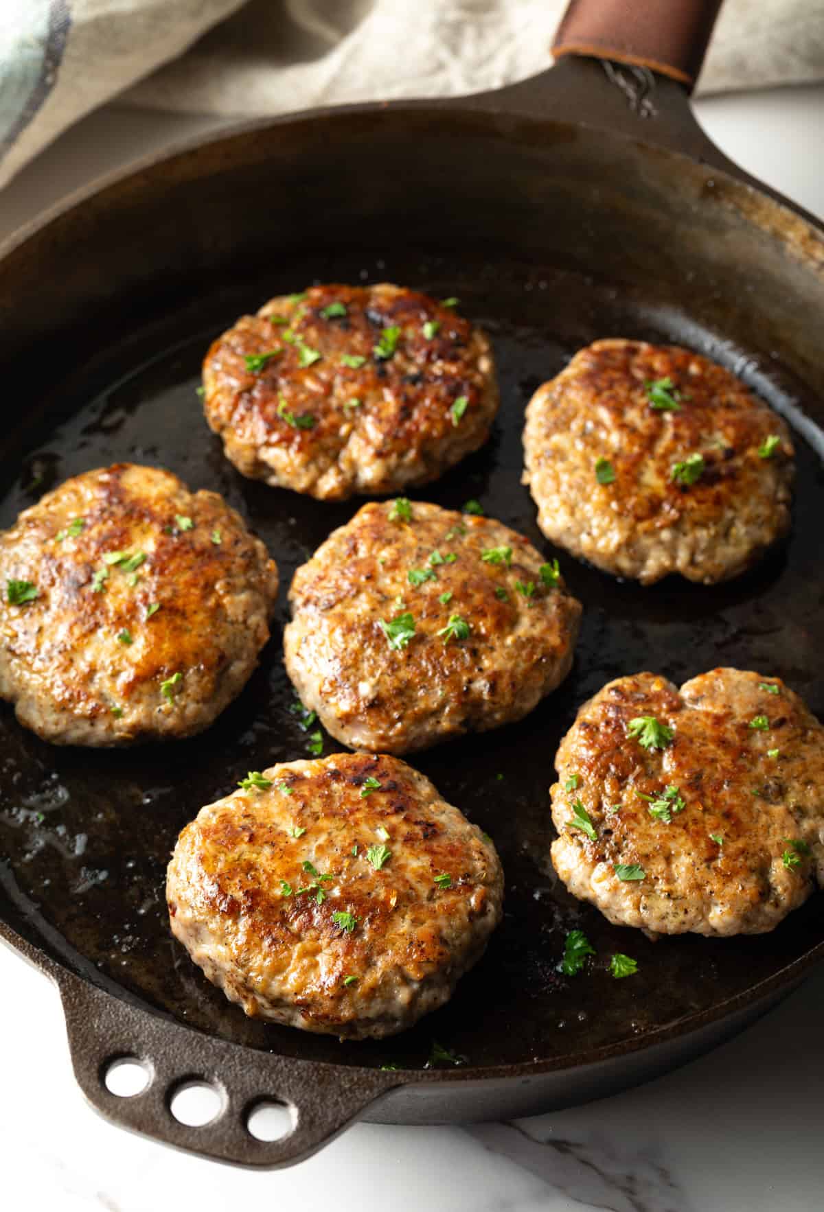 Homemade breakfast sausage patties are being cooked and browned in a black skillet.