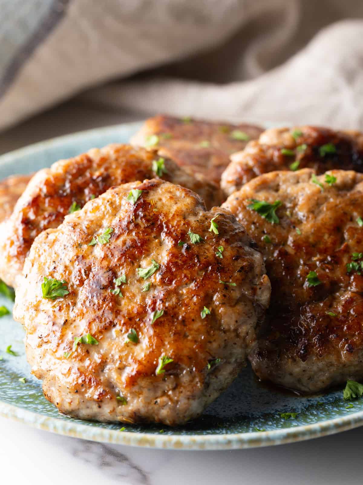 Slices of easy homemade breakfast sausage patties are lined up in a circle on a blue plate.