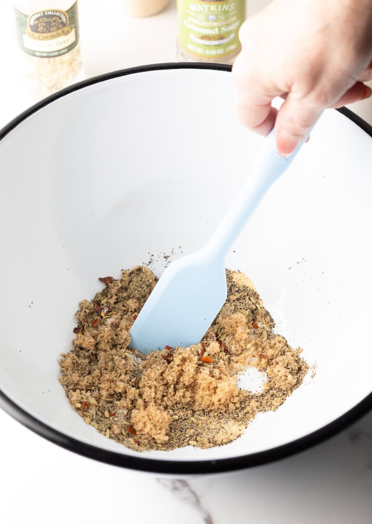A mix of herbs and spices being stirred in a white bowl with a spatula.