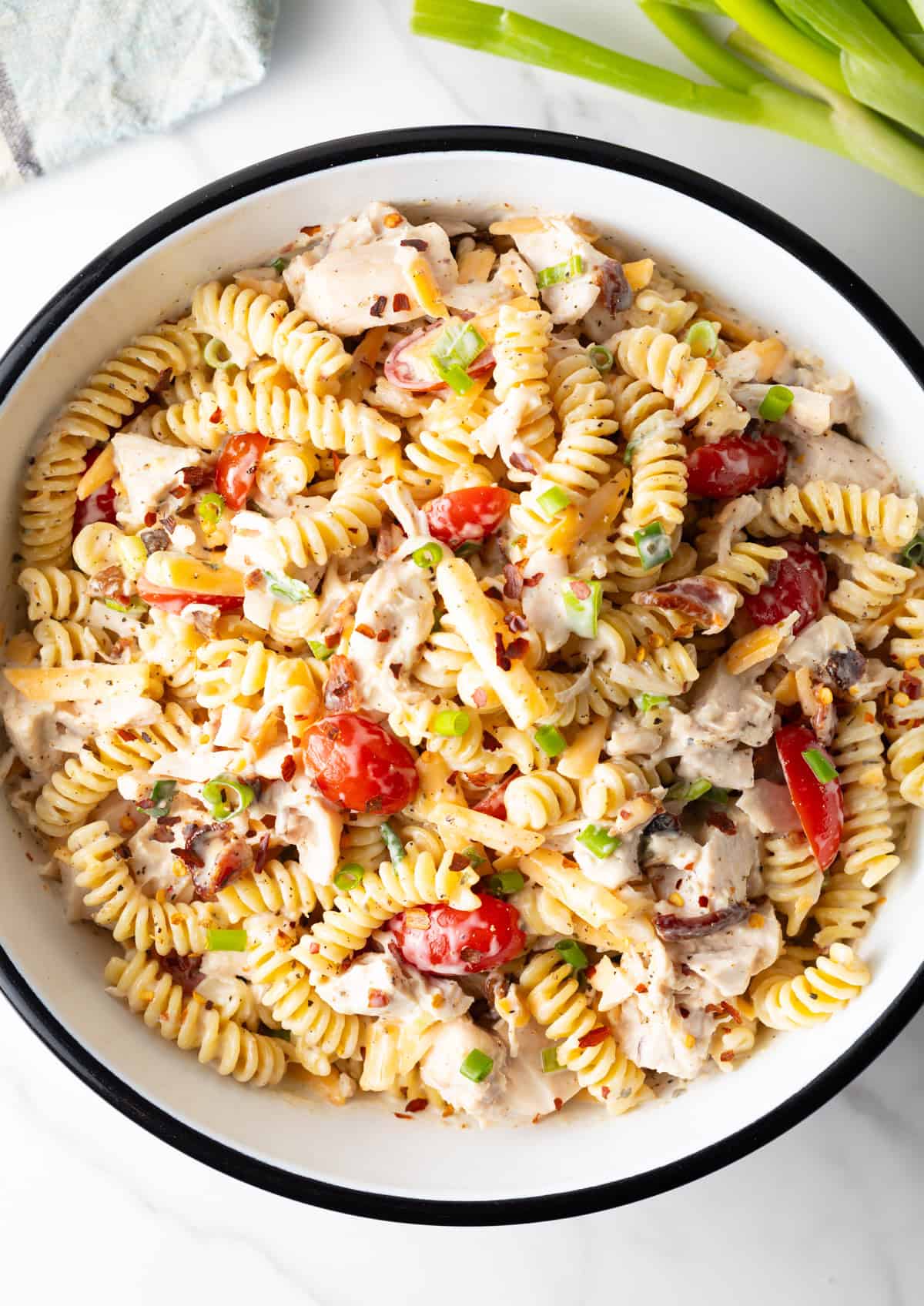 An overhead shot of a white bowl filled with creamy chicken bacon ranch pasta salad with fusilli, bacon, and tomatoes.