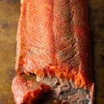 A fillet of cold smoked salmon with a piece flaked off, sitting on a brown surface.