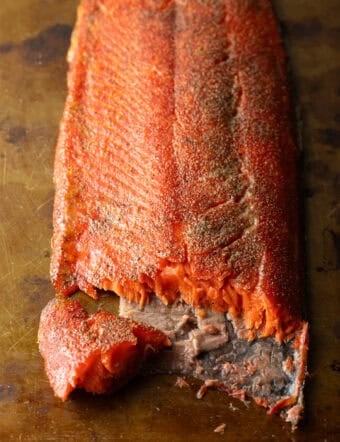 A fillet of cold smoked salmon with a piece flaked off, sitting on a brown surface.