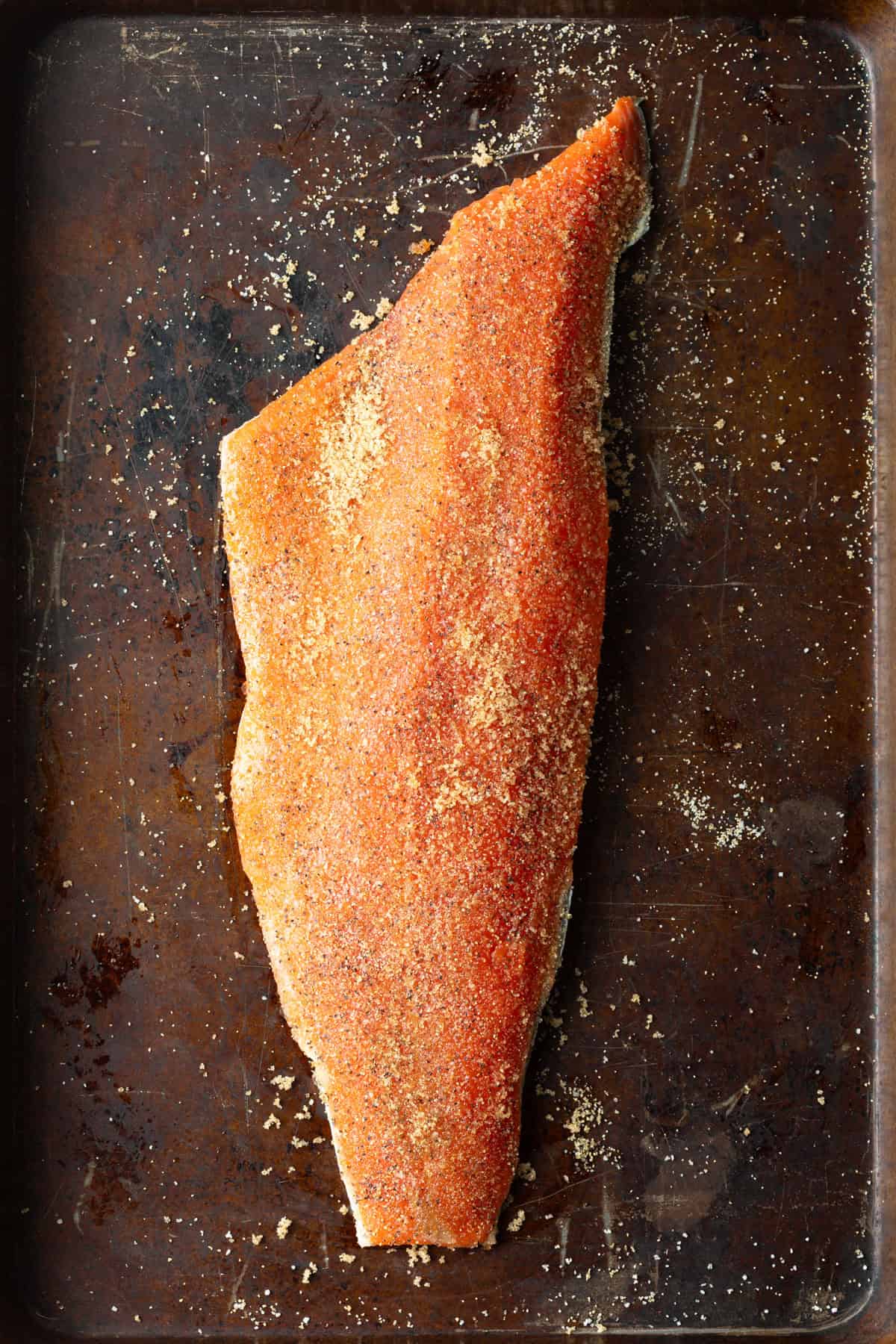 A whole fillet of raw salmon that has been sprinkled with seasoning, sitting on a baking tray.