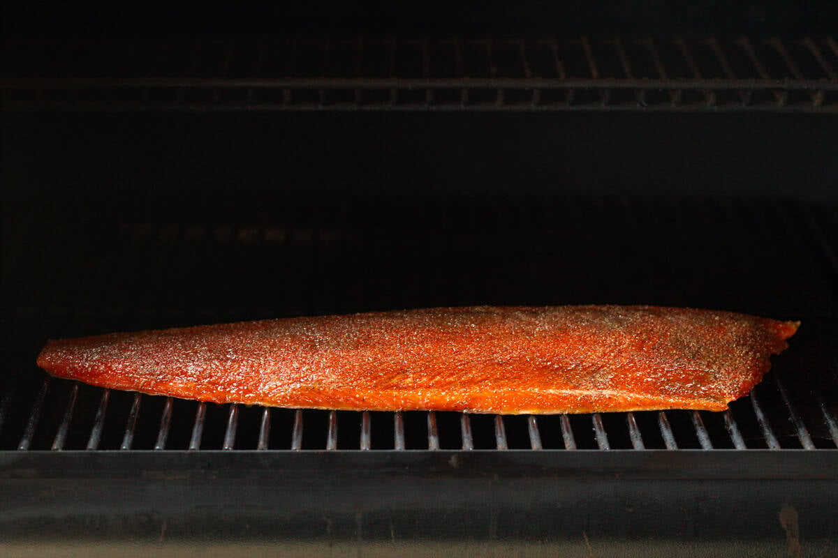 A whole fillet of salmon is sitting on a metal smoker grate, being prepared for an easy smoked salmon recipe.