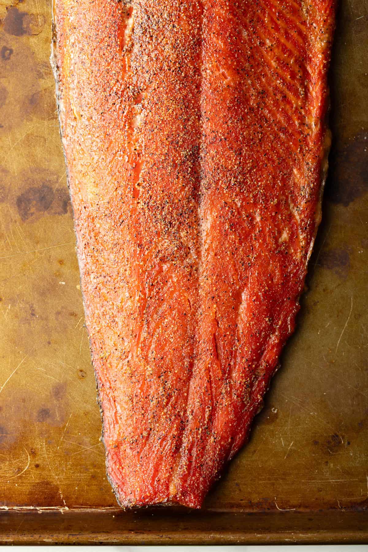 A whole fillet of homemade smoked salmon sitting on a brown surface.