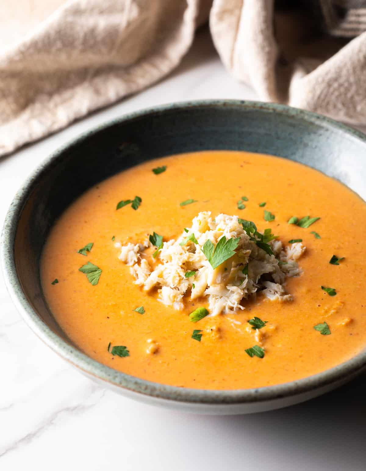 A grey bowl filled with a creamy crab bisque soup recipe, with crab meat and parsley on top.