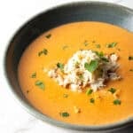 A black bowl filled with creamy crab bisque soup with crab meat and parsley on top.