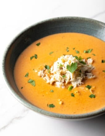 A black bowl filled with creamy crab bisque soup with crab meat and parsley on top.