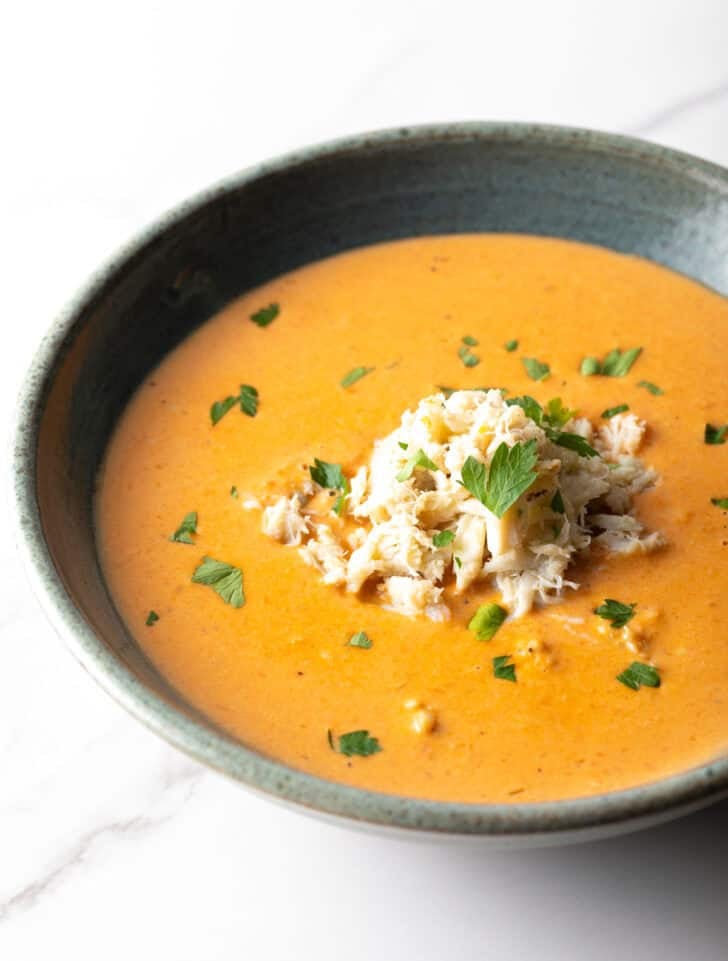 A black bowl filled with creamy crab bisque soup with crab meat and parsley on top.