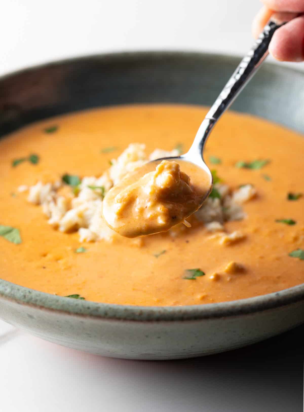 A spoon with a bite of crab bisque soup is being held over a bowl of the soup.