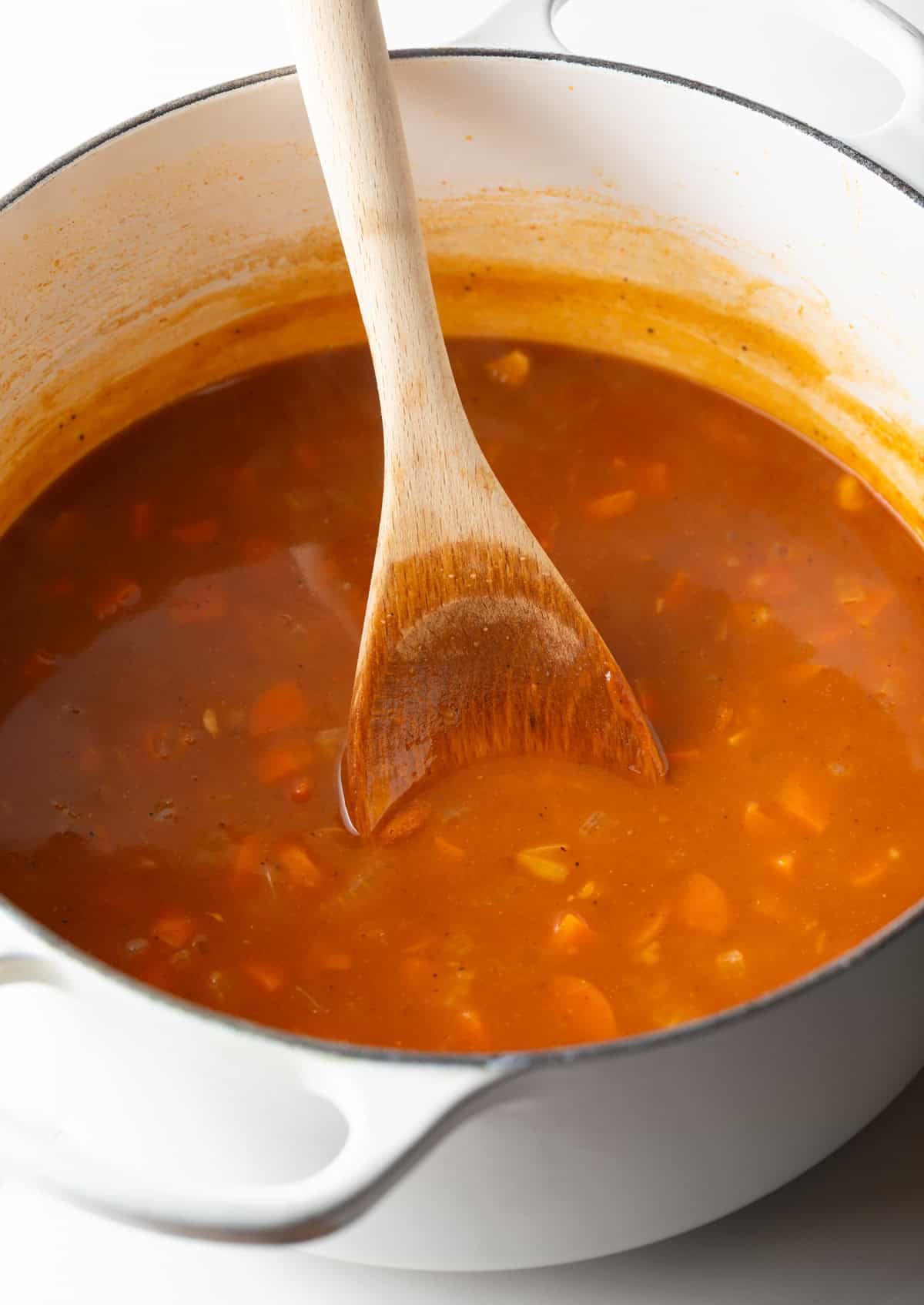 A crab bisque soup base is being simmered and stirred in a white pot.