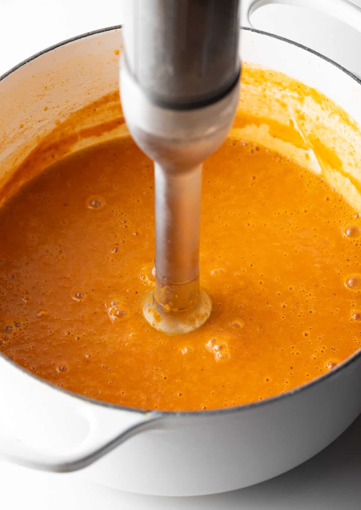 An immersion blender is blending a crab bisque soup base.