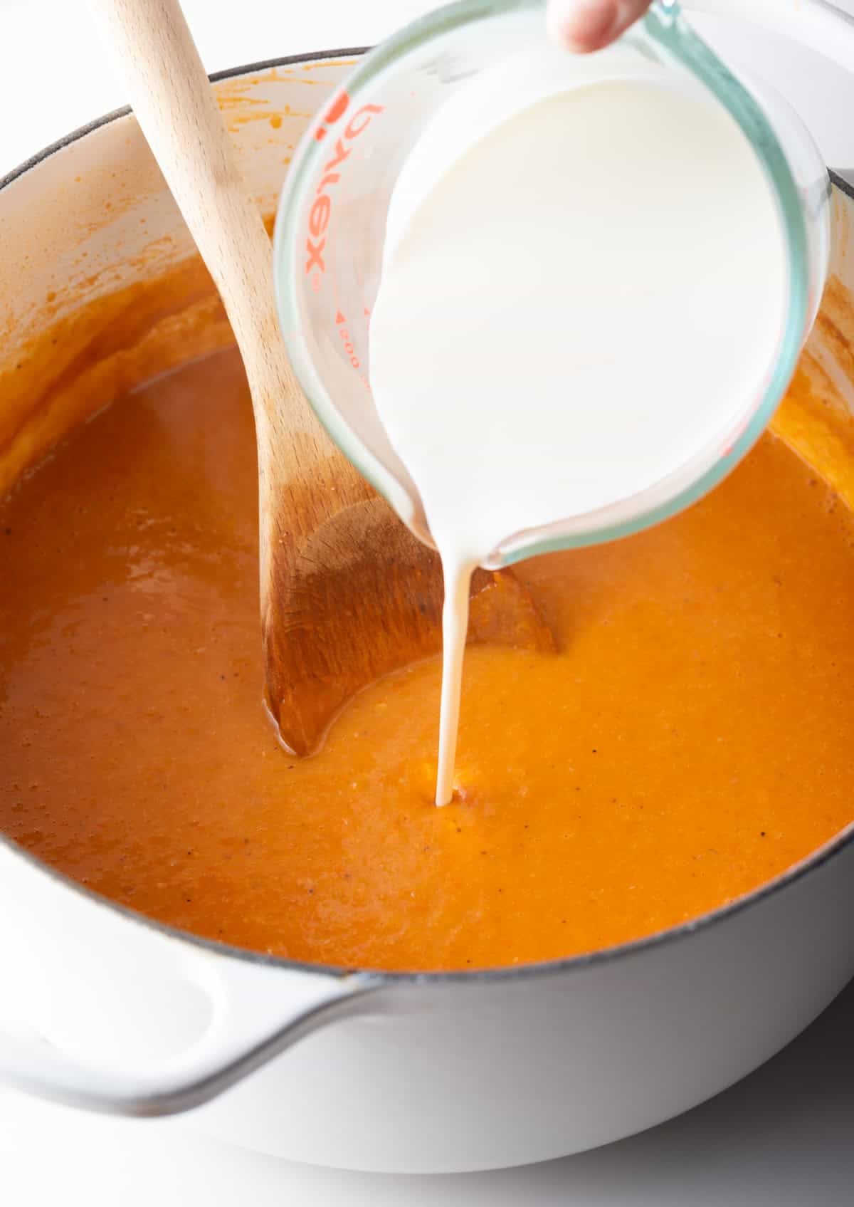 Heavy cream is being added to a crab bisque recipe soup base.