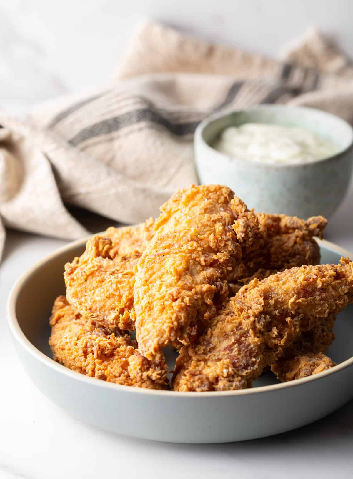A white bowl filled with deep fried chicken tenders, with a ramekin of white sauce on the side.