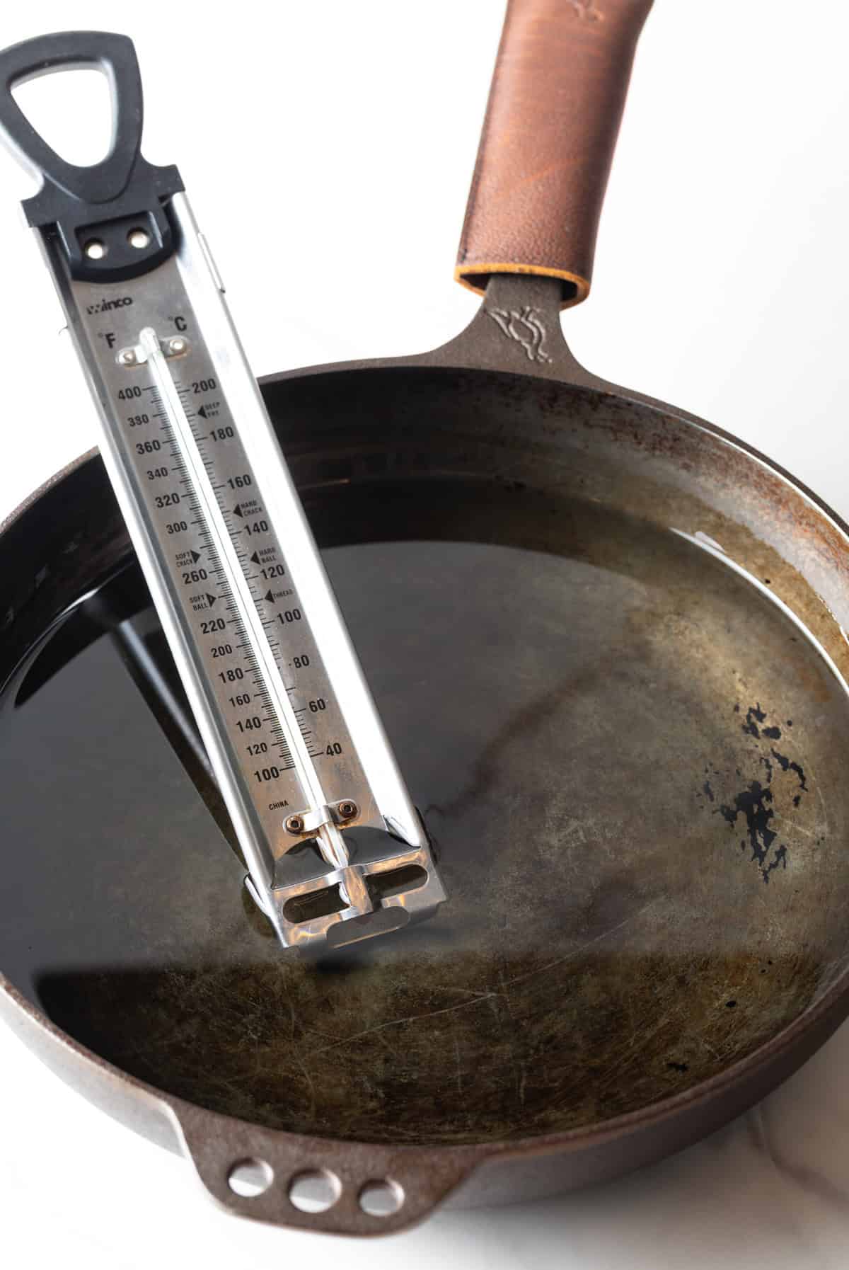 A cooking thermometer is being used in a black skillet filled with cooking oil.