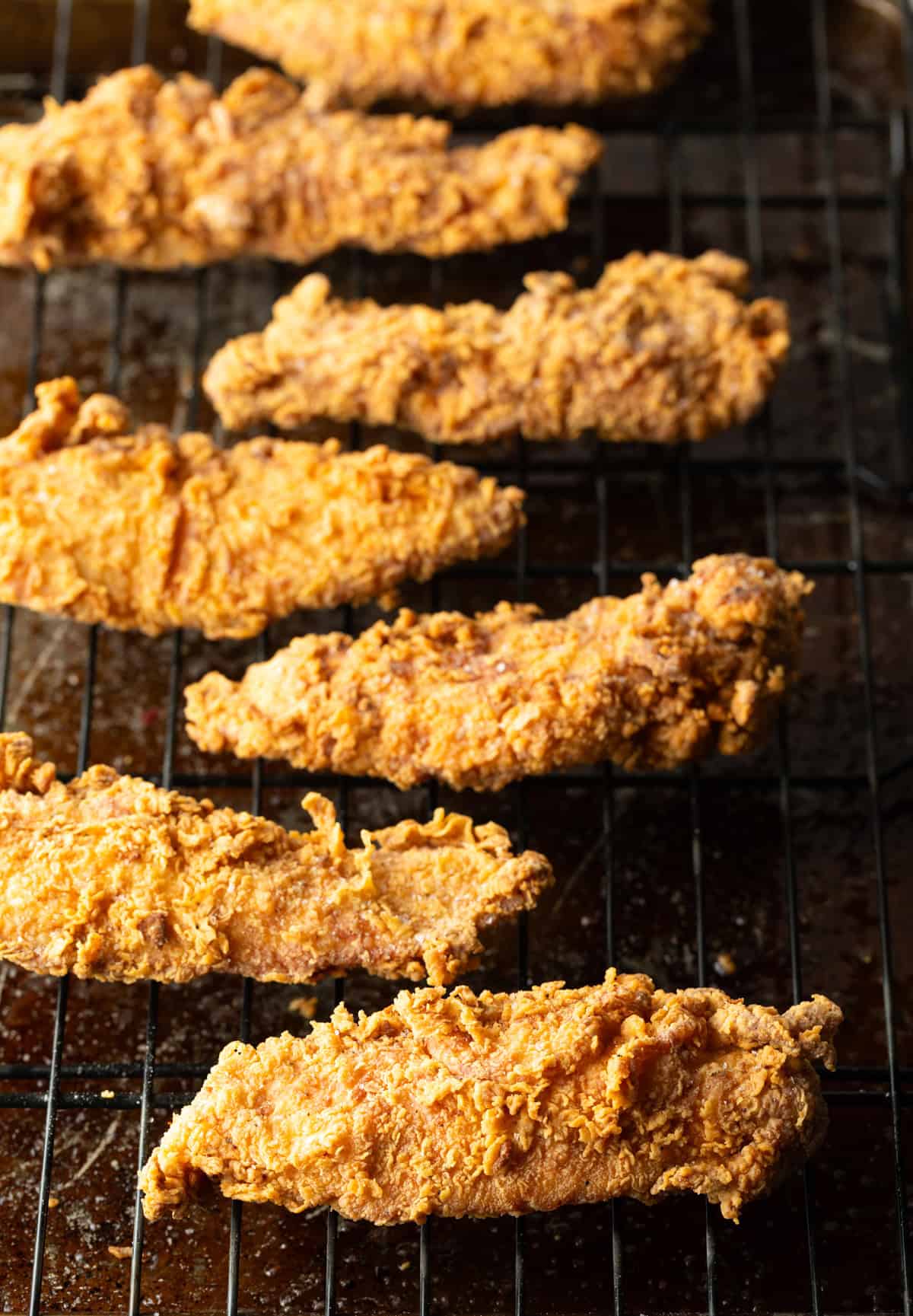 Crispy pan fried chicken tenders sitting on a metal drying rack.