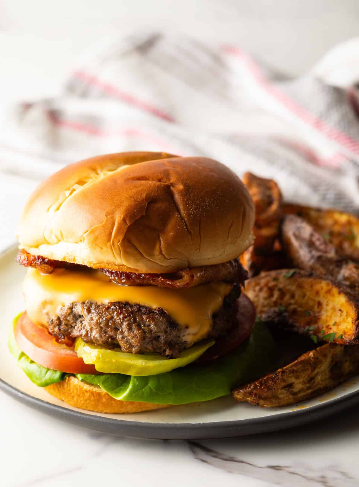A deer burger recipe topped with melted cheese, sitting on a plate with potato wedges.
