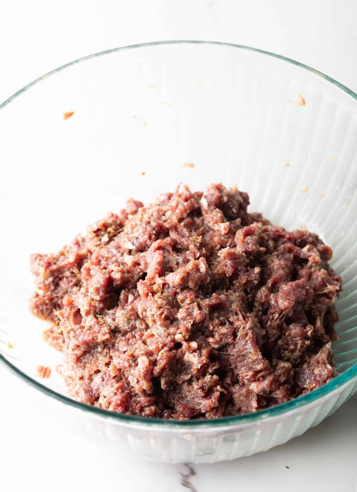 A meat mixture for a deer hamburger recipe is in a glass bowl.