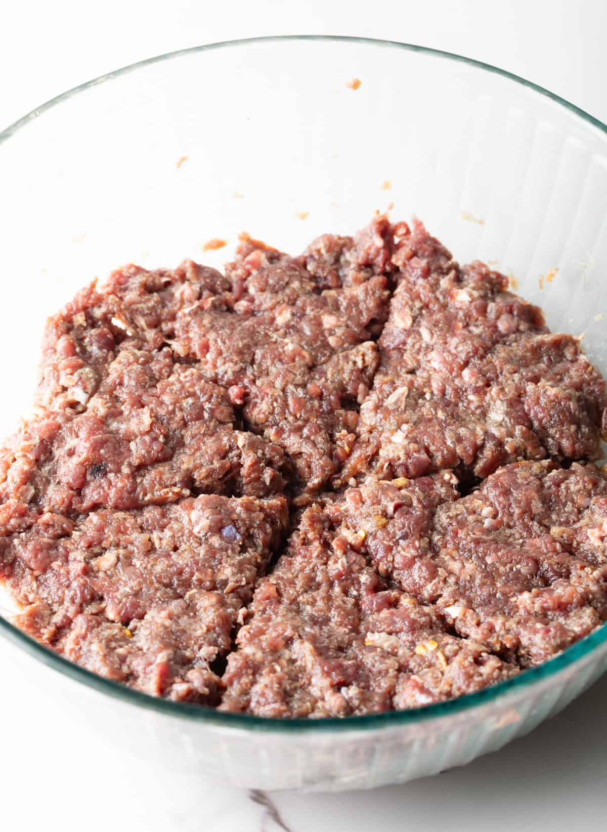 A homemade deer burger recipe mixture in a glass bowl, sectioned into 6 servings and ready to be formed into burger patties.