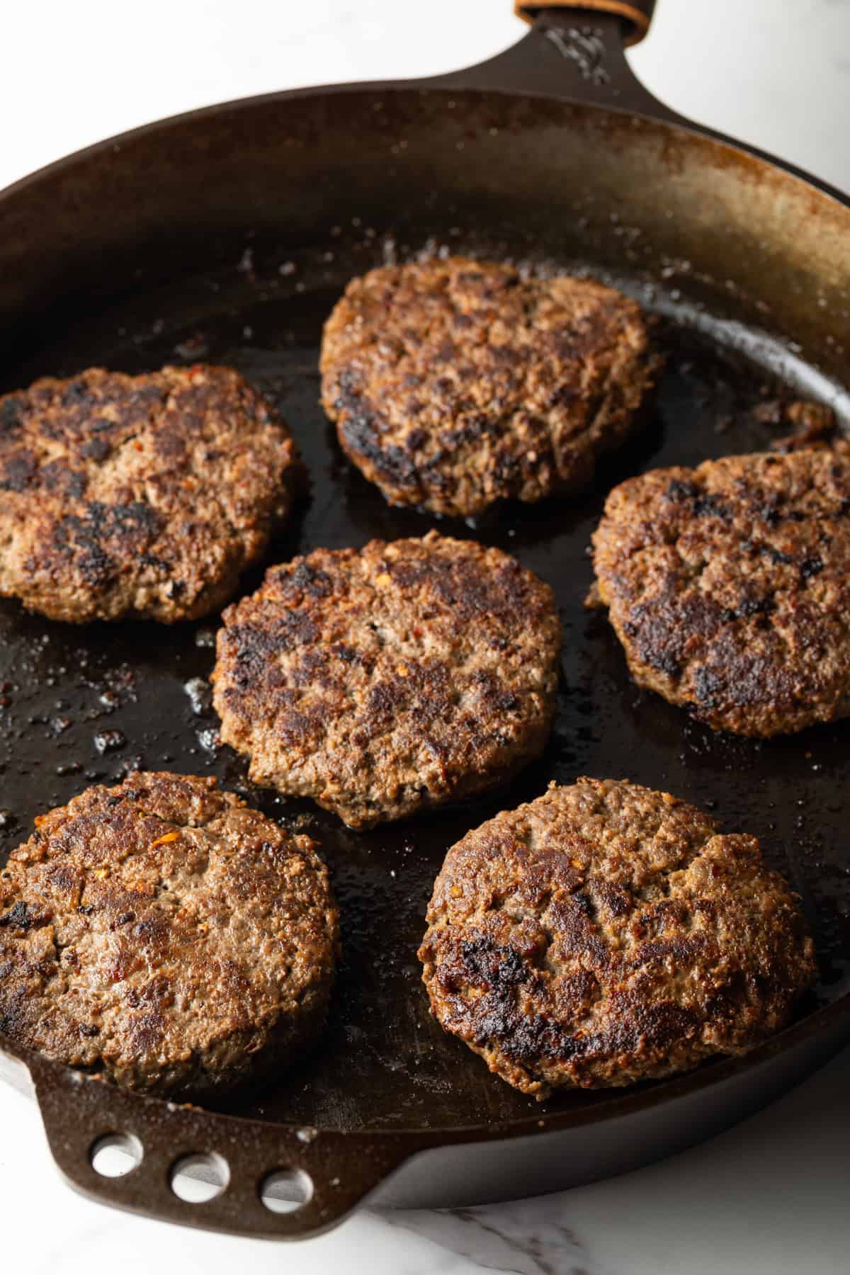 Deer burger patties are being grilled in a black skillet.