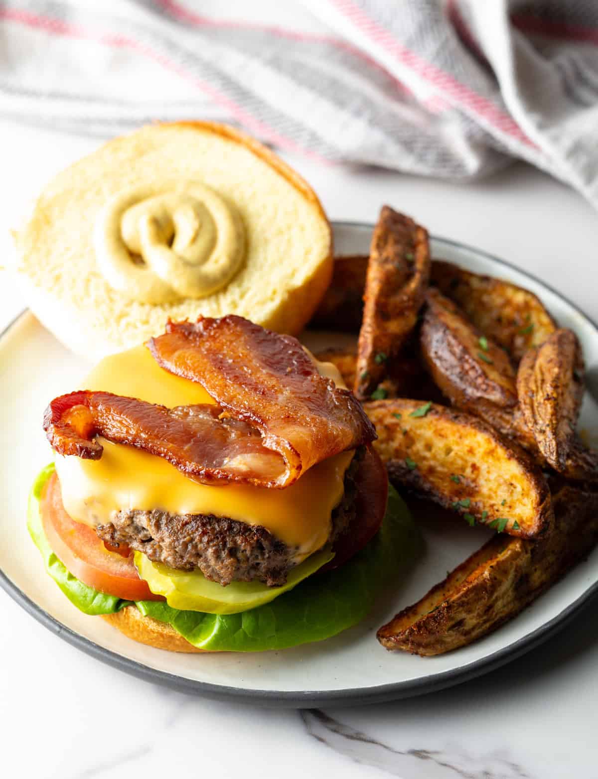 An deer hamburger with the top bun off, showing it is topped with cheese and bacon.