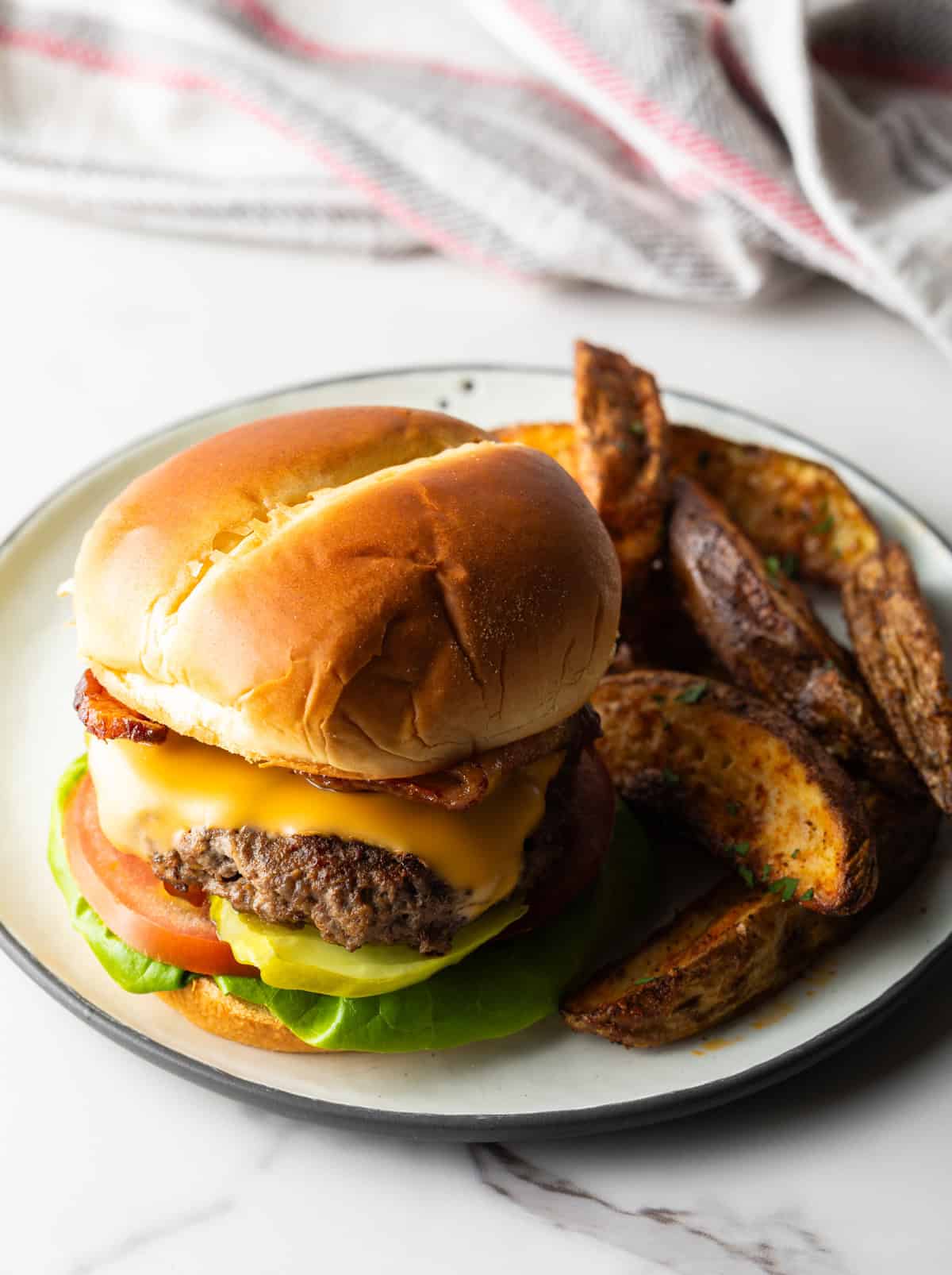 A deer hamburger recipe topped with melted cheese, sitting on a plate with potato wedges.