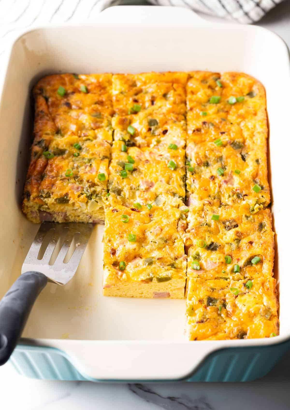 Pre-sliced western omelette casserole in a white baking dish, with a metal spatula ready for serving.