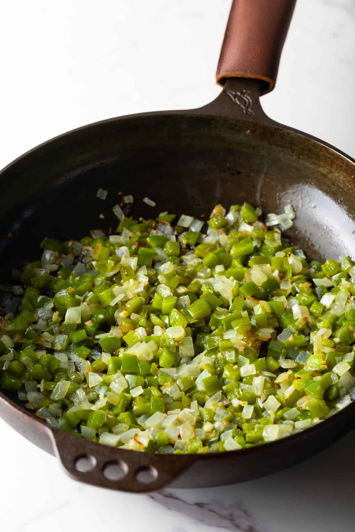 Diced vegetables for a baked omelet casserole are being sautéed in a black skillet.