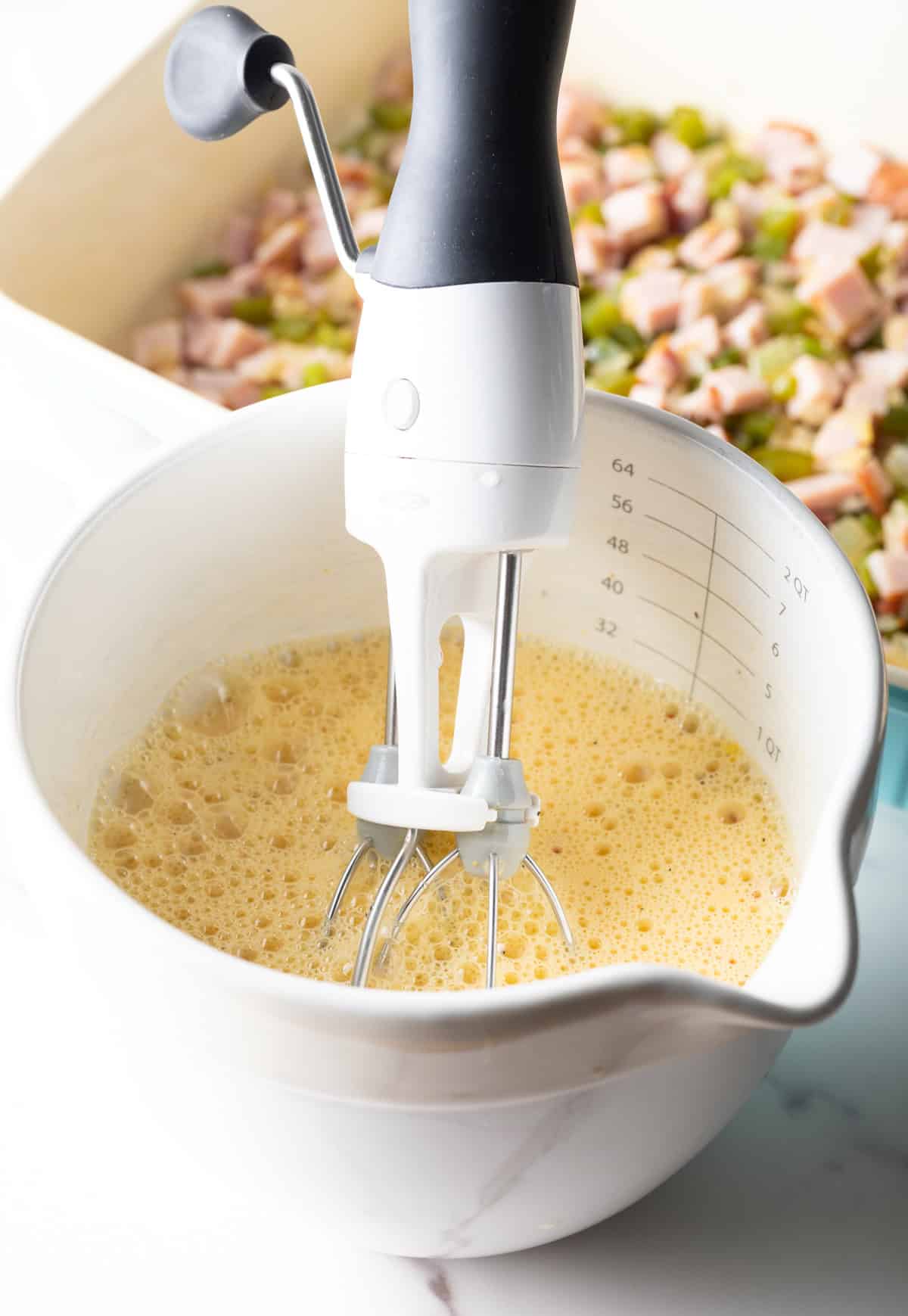 An egg and cream mixture is being whisked together in a white measuring bowl.