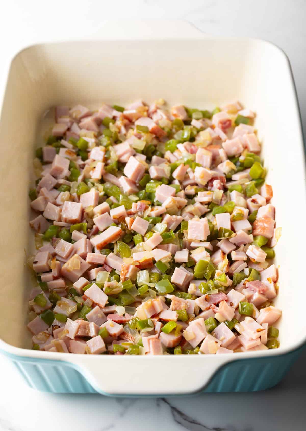 Cubed ham and diced veggies layered at the bottom of a white baking dish.