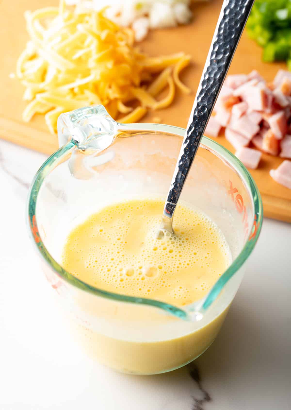 An egg and cream mixture is being mixed in a glass measuring bowl.