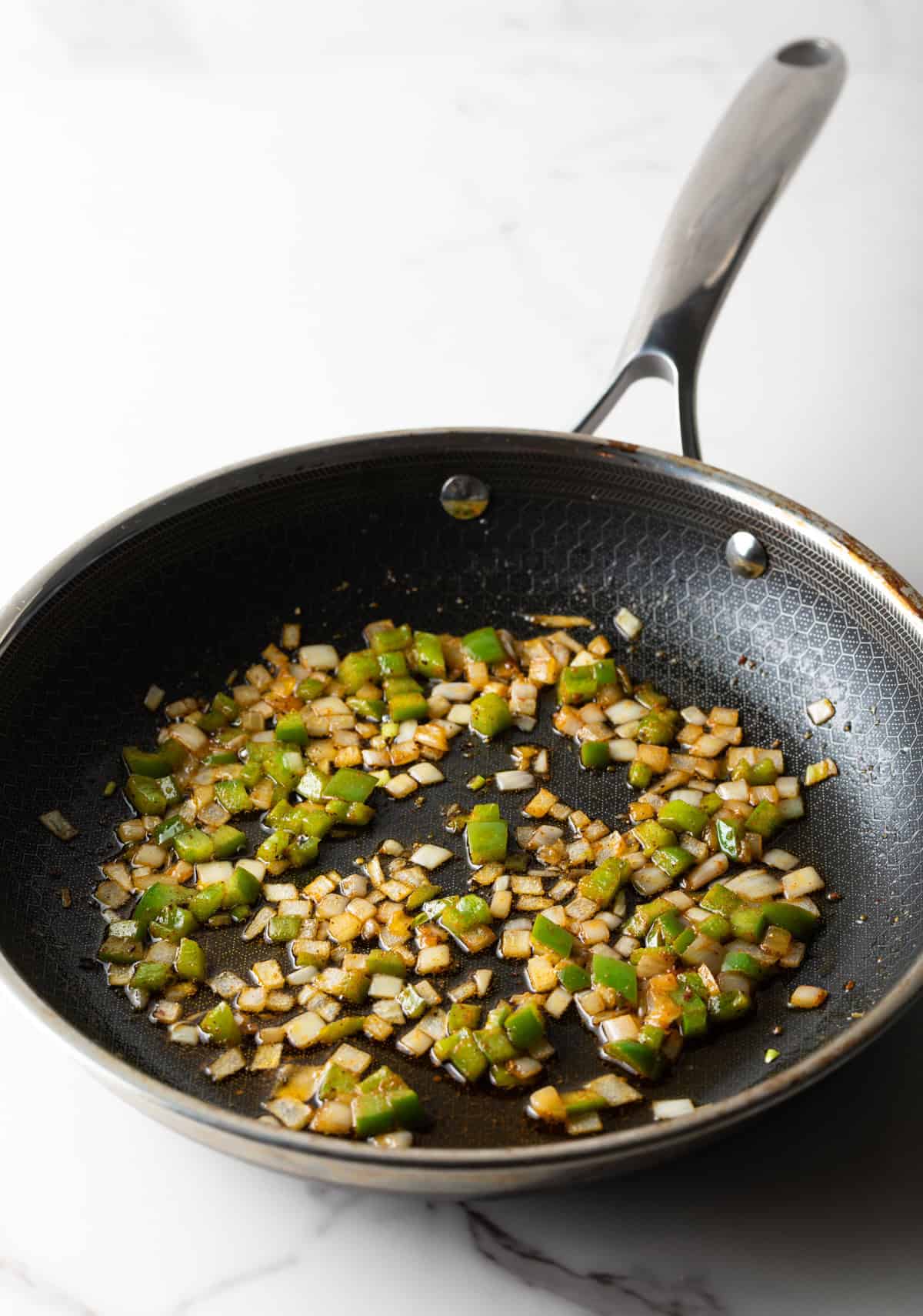 Diced onion and green peppers are being sautéed in a black pan.