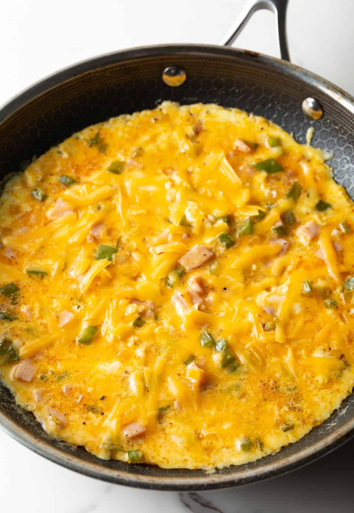 Shredded cheese is being melted on top of a Denver omelet recipe in a black skillet.