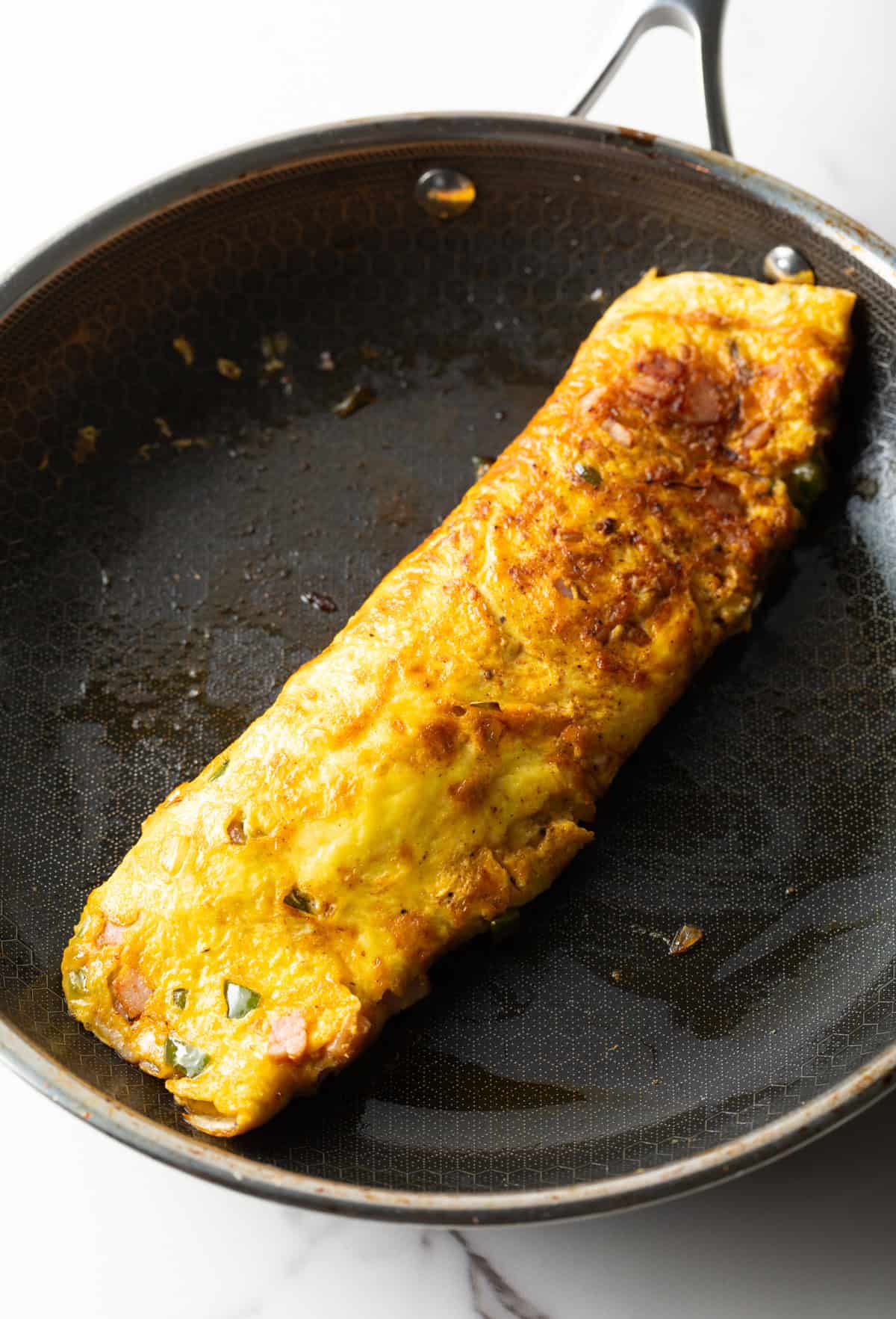 A Denver omelette recipe is being folded in a black skillet.