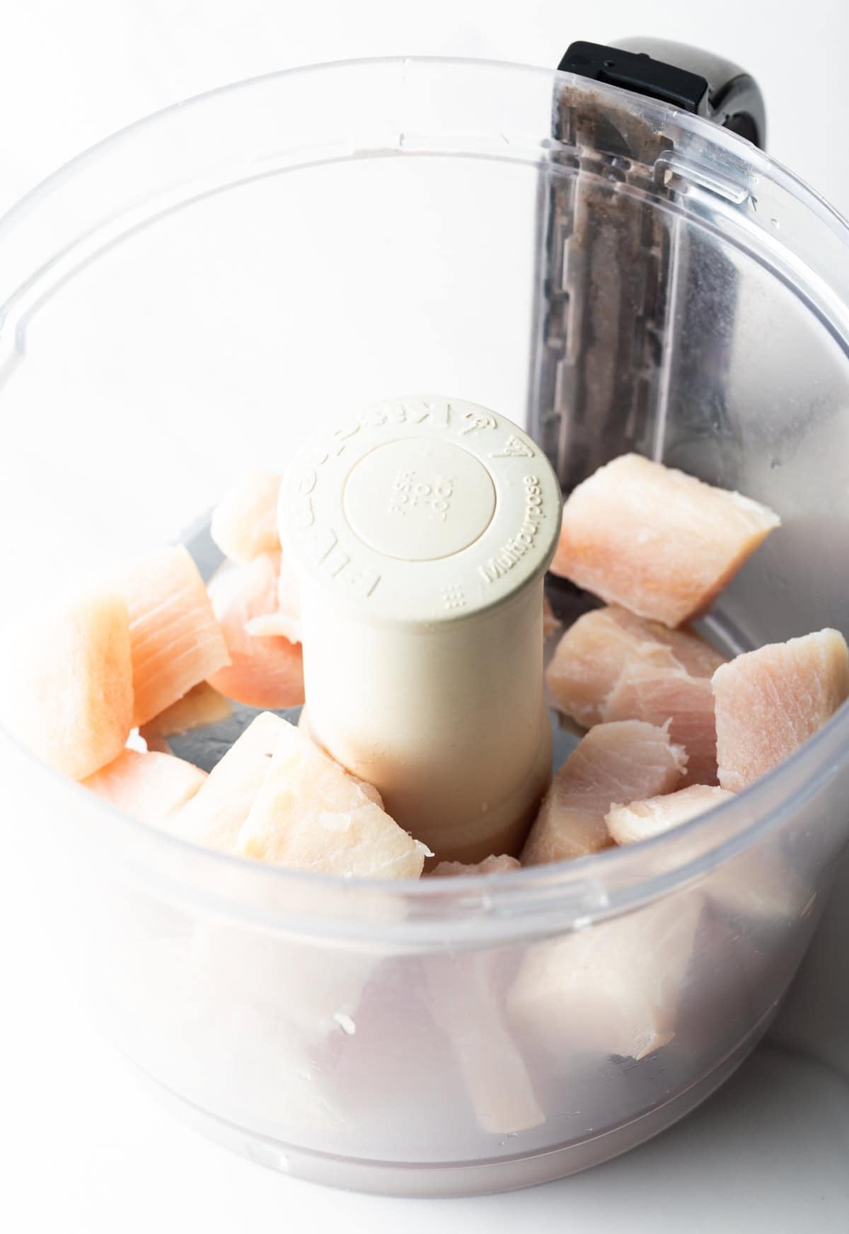 Chunks of raw white fish are sitting in a food processor for a fish burger recipe.