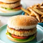 A homemade fish burger with lettuce and tomato on a blue plate, with a plate of fries on the side.