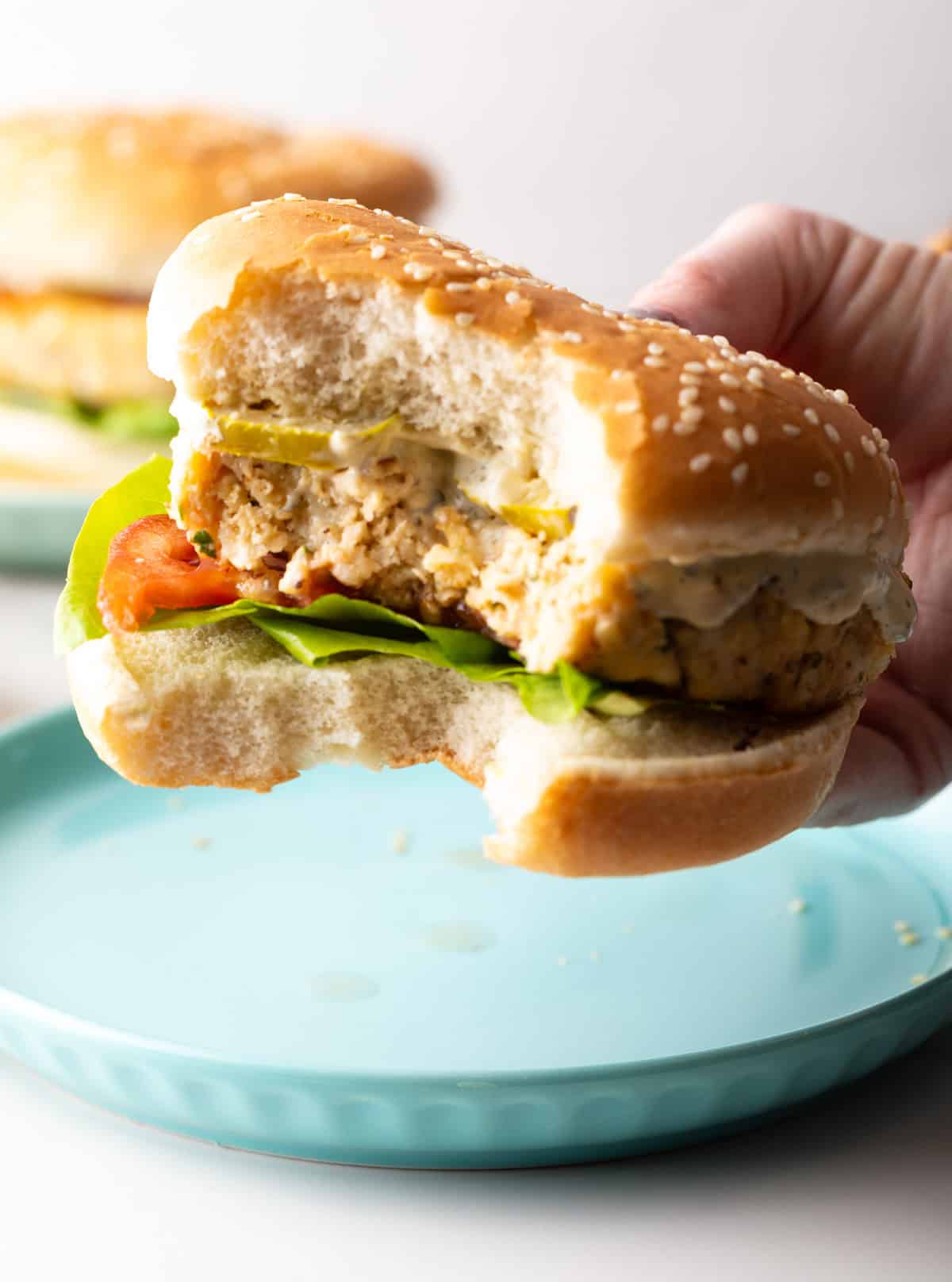 A hand is holding a recipe for fish hamburgers with a bite taken out.