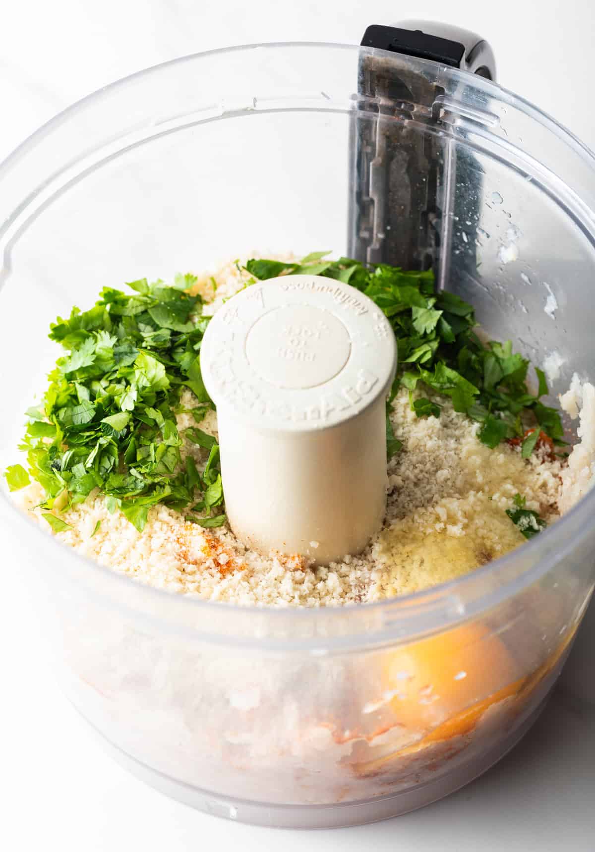 Egg, mayonnaise, and seasonings are being added to a food processor with white fish.