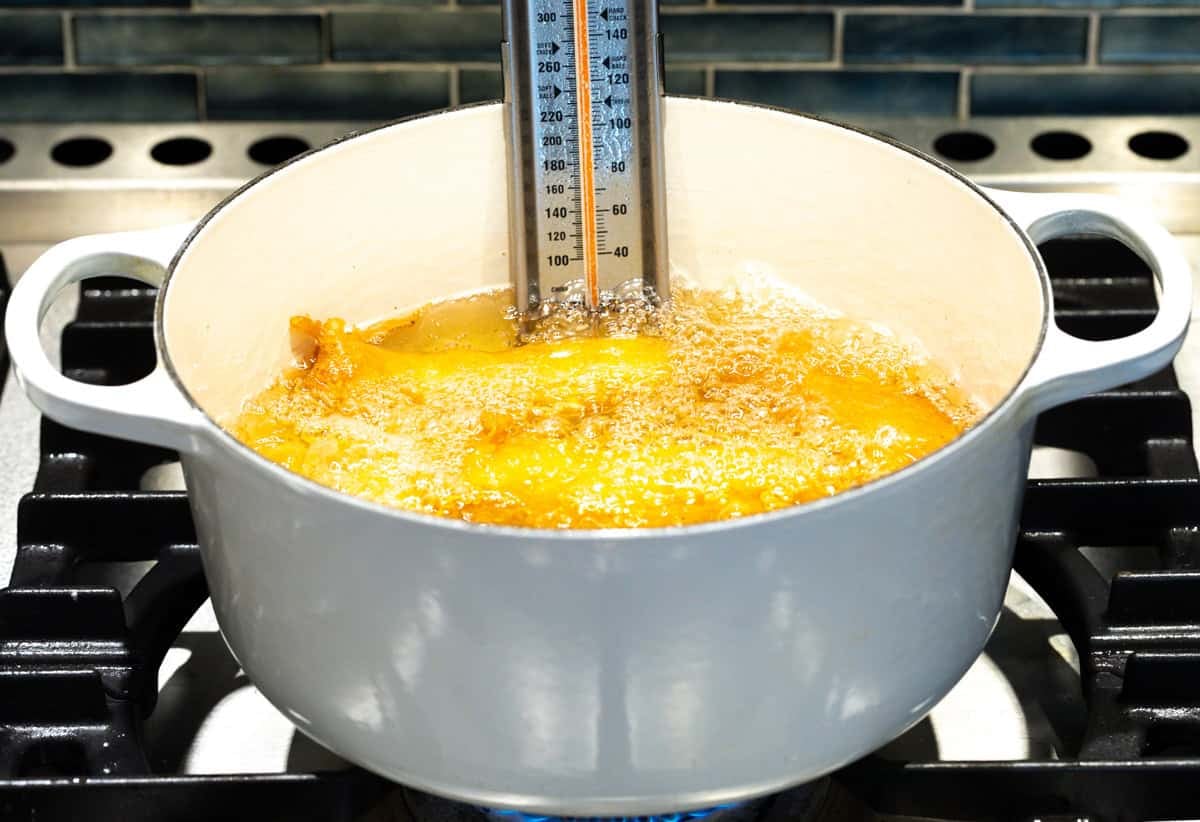 Battered fish filets are frying in a pot filled with oil and a cooking thermometer.